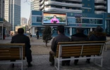 Des Nord-Corénes, assis sur un banc dans une rue de Pyongyang le 1er mars 2019, regardent sur un écran géant la speakrine officielle donner des informations sur la rencontre entre le président américain Donald Trump et leur leader Kim Jong Un à Hanoï