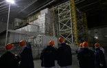 Des représentants de Greenpeace et des médias devant le sarcophage recouvrant le quatrième réacteur détruit sous l'enceinte de confinement, à la centrale nucléaire de Tchernobyl, le 9 avril 2026 en Ukraine