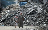 Un Palestinien tient un enfant par la main alors qu'ils passent devant un bâtiment rasé par les bombardements israéliens dans le camp de réfugiés de Bureij, dans le centre de la bande de Gaza, le 25 août 2024
