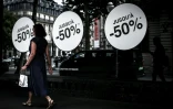 Une passante marche à côté d'une vitrine annonçant les soldes, le 25 juin 2025 à Paris