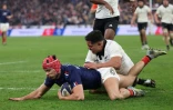L'ailier gauche français Louis Bielle-Biarrey (C) plonge pour marquer le troisième essai français alors qu'il est plaqué par le centre néo-zélandais Anton Lienert-Brown (R) lors de la tournée d'automne entre la France et la Nouvelle-Zélande au Stade de France, le 16 novembre 2024