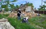Une femme transporte quelques effets personnels dans une poussette près d'une maison détruite dans le village de Vilkhivka, près de Kharkiv, le 25 mai 2022
