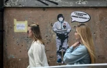 Deux femmes passent devant un message mural où il est écrit: "Il y a une épidémie d'ignorance dans l'air, nous devons nous protéger", par l'artiste Laika, près du quartier chinois de Rome, le 4 février 2020