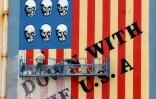 Un homme repeint un mur de l'ancienne ambassade des Etats-Unis à Téhéran le 8 avril 2025, aux couleurs du drapeau américain avec des têtes de mort remplaçant les étoiles