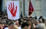 Des personnes défilent derrière une banderole ornée d’une main rouge lors d’une manifestation antigouvernementale à Belgrade, le 23 mai 2026, dénonçant la corruption et réclamant des élections anticipées après l’effondrement meurtrier de l'auvent de la gare de Novi Sad, en Serbie, en 2024
