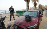 Un policier observe une voiture endommagée sur le site d'une frappe aérienne israélienne dans la zone côtière de Ramlet al-Bayda à Beyrouth, le 12 mars 2026 au Liban