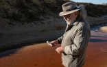 David van Wyk, chercheur principal à la Bench Marks Foundation, effectue des tests dans un cours d'eau à la décharge de la mine de Snake Park, à Soweto, le 30 mai 2025 en Afrique du Sud