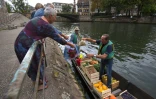 Christophe Moegling (G), et l'un de ses employés vendent des fruits et des légumes depuis la barque à fond plat faisant office de marché flottant sur la rivière de l'Ill à Strasbourg (est), le 6 septembre 2017