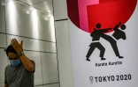 Un passant, portant un masque chirurgical, près d'une affiche liée à l'épreuve de karaté des Jeux de Tokyo, le 12 juin 2020 dans l'arrondissement de Shinjuku.