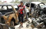 Un homme marche près de voitures endommagées après un attentat-suicide du groupe EI à un barrage menant à Husseiniyah au nord-est de Bagdad le 13 juillet 2016