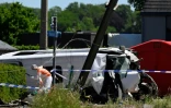 Un membre de la police scientifique inspecte les lieux à côté d'un bus endommagé après avoir été percuté par un train au passage à niveau de Vierhuizen à Buggenhout, au nord de Bruxelles, le 26 mai 2026 en Belgique