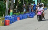 Une moto passe devant une file de bombonnes en plastique placées par des habitants qui attendent des livraisons d'eau dans la ville de Bogo, dans la province de Cebu aux Philippines, le 2 octobre 2025