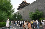 Une femme en robe traditionnelle (g) pose pour une photo alors que des touristes visitent la Cité Interdite à Pékin, le 11 juillet 2026