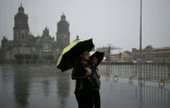 Un homme marche sous la pluie sur la place du Zocalo dans le centre de Mexico le 30 septembre 2024 à la veille de la cérémonie d'investiture de la nouvelle présidente Claudia Sheinbaum
