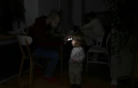 Un habitant de Kiev aide sa fille de deux ans à utiliser une lampe frontale dans leur appartement lors d'une coupure de courant à Kiev, le 13 janvier 2026