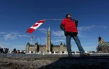 Un homme porte un drapeau canadien près de la colline du Parlement, où se trouvent des manifestants opposés aux mesures sanitaires de Justin Trudeau, le 7 février 2022 à Ottawa