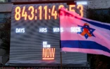 Un drapeau israélien orné d'un ruban jaune devant l'horloge comptabilisant les jours, les minutes et les secondes écoulées depuis l'enlèvement d'otages israéliens vers la bande de Gaza lors des attaques du 7 octobre 2023, à Tel-Aviv, le 27 janvier 2026