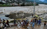 Des personnes se rassemblent devant une route endommagée par les eaux de crue suite aux fortes pluies de mousson dans la région de Madian, dans la vallée de Swat, au nord du Pakistan, le 27 août 2022