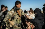 Un combattant des Forces démocratiques syriennes oriente une femme portant un bébé et qui attend d'être fouillée après avoir quitté le dernier réduit du groupe Etat islamique à Baghouz, dans l'est de la Syrie, le 1er mars 2019 