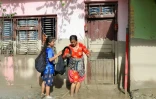 Des femmes devant une maison portant des traces de boue indiquent le niveau de l’eau après des crues dévastatrices près de Devighat, au Népal, le 27 août 2026