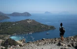 Une touriste sur le bord du cratère de La Fossa, sur l'île de Vulcano, avec (g-d) les îles de Lipari, Panarea et Stromboli, dans l'archipel des Éoliennes, au large de la Sicile, le 9 juillet 2026 en Italie