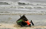 Des hommes poussent un bateau de pêche à titre préventif lors des pluies à Kuakata le 26 mai 2024, avant l'arrivée du cyclone Remal dimanche soir au Bangladesh.