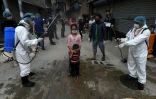 Des agents sanitaires aspergent des enfants d'une solution désinfectante, le 7 mai 2020 à Katmandou, au Népal