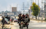 Des hommes à l'arrière d'un tricycle le long de la route de Salaheddin à Deir al-Balah, dans le centre de la bande de Gaza, le 21 juillet 2025, tandis que derrière eux s'élèvent des volutes de fumée provenant des bombardements israéliens