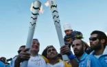 Le président du comité héllenique olympique, Spyros Kapralos (gauche) remet la flamme olympique au réfugié syrien Ibrahim al-Hussein (centre), un nageur amputé, le 26 avril 2016 à Athènes