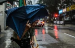Un vieil homme attend un taxi en tentant de se protéger des intempéries à Hong Kong le 16 septembre 2018. 