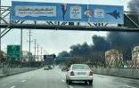 Des véhicules roulent sur une autoroute le long de laquelle s'élève un épais nuage de fumée à Téhéran, cible de frappes aériennes israélo-américaines, le 8 mars 2026