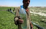 Un homme tient une bouteille d'eau près d'une pompe acheminant de l'eau du lac Assad, le 25 juillet 2021 à Roumeilia, dans le nord de la Syrie