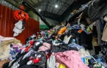 Sur cette photo prise le 7 août 2024, un employé manie une pince mécanique pour trier une énorme pile de vêtements, de draps, d'accessoires et de peluches avant leur exportation, dans une usine de vêtements de seconde main à Paju, au nord de Séoul