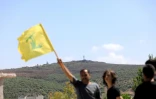 Un homme brandit le drapeau du parti Hezbollah, avec une position militaire israélienne (en arrière-plan), dans le village d'Aïta al-Chaab, dans le sud du Liban, près de la frontière avec le nord d'Israël, le 29 juin 2024