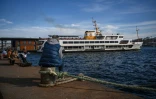Un ferry est amarré au port de Karakoy à Istanbul alors que des gens sont assis sur la rive du Bosphore, le 8 février 2021 à Istanbul.