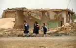 Des écolières passent devant une maison détruite à Habach, dans le nord de l'Irak, le 25 avril 2022 
