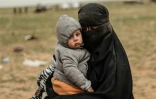 Une mère portant son enfant attend d'être fouillée par les Forces démocratiques syriennes après avoir fui le dernier réduit du groupe Etat islamique à Baghouz en Syrie, le 27 février 2019