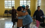 Baile Bantseke (c,g), grand-mère d'un enfant autiste, enlace Lilly Stebe (c,d), mère adoptive d'une enfant atteinte de paralysie cérébrale, lors d'une réunion du Snake Park Cerebral Palsy Forum à Soweto, le 23 mai 2025 en Afrique du Sud