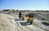 Des villageois acheminent des bidons d'eau sur des brouettes dans le village de Bolak, dans le nord de l'Afghanistan, le 10 juillet 2025 