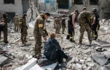 Iaroslava (au centre), 51 ans, qui pense que son mari est sous les débris,  est assise sur son sac pendant que les secours inspectent les lieux, à Sydorovié (est de l'Ukraine), le 17 mai 2022