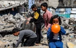 Une petite fille gonfle un ballon pendant que des garçons fouillent les décombres d'un bâtiment détruit à Rafah, dans le sud de Gaza, le 5 avril 2024