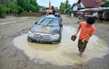 Un homme passe devant une voiture embourbée à la suite de crues soudaines à Meureudu, dans la province d’Aceh, en Indonésie, le 28 novembre 2025