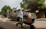 Une femme pousse une brouette chargée d'un bidon d'eau tandis qu'une voiture de l'armée nigériane patrouille dans la ville de Banki, dans le nord-est du Nigeria, le 26 avril 2017