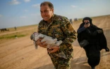 Un membre de la force antijihadiste arbo-kurde porte un bébé suivie par une femme qui vient de quitter le dernier réduit du groupe Etat islamique (EI) près de Baghouz, dans l'est de la Syrie, le 22 février 2019