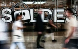Des passants passent devant la porte d'entrée d'un grand magasin où est accrochée une affiche annonçant les soldes d'été à Paris, le 25 juin 2025