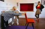 Dorothea Barron, 100 ans, vétérane britannique de la Seconde Guerre mondiale, aide une élève à étirer son dos lors d'un cours de yoga près de Harlow, le 31 mars 2025 au nord de Londres
