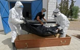 Des employés municipaux mettent le corps d'une victime du Covid-19 dans un cercueil dans un hôpital de Kairouan, en Tunisie, le 4 juillet 2021