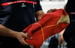 Un pompier avec "en grève" scratché sur la poitrine, devant l'hôtel de Beauvau présente une cagoule anti-feu à Paris, le 13 août 2026
