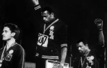 Tommie Smith (c) et John Carlos, poings gantés et levés vers le ciel, manifestent sur le podium du 200 m des Jeux de Mexico, le 16 octobre 2018