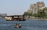 Une famille de pêcheurs assise dans un bateau face à une péniche amarrée sur l'une des rives du Nil entre le quartier Zamalek et le quartier Agouza le 27 juin 2022